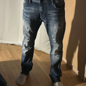Blå jeans med slitningar - Snygga blå jeans med coola slitningar på framsidan. De har en klassisk femficksdesign och en bekväm passform. Perfekta för en avslappnad stil.