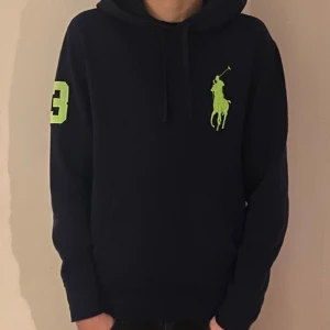 Mörkblå hoodie från Polo Ralph Lauren - Säljer en snygg mörkblå hoodie från Polo Ralph Lauren med en stor grön logga på bröstet och siffran 3 på ärmen. Perfekt för en casual look. Tillverkad i en bomulls- och polyesterblandning för extra komfort.
