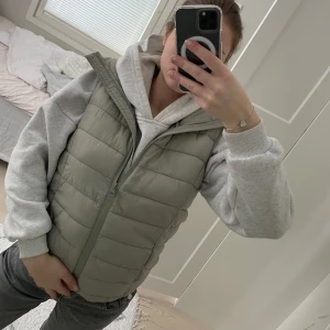 Grön dunväst - Säljer en stilren grön dunväst. Perfekt för lager-på-lager under kyligare dagar. Västen har en enkel design som gör den lätt att matcha med olika outfits.