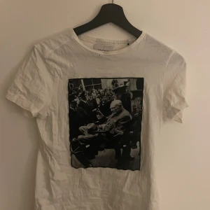 Vit t-shirt med tryck från Limitato - Säljer en vit t-shirt från Limitato med ett svartvitt tryck på framsidan. T-shirten är kortärmad och tillverkad i bomull. Perfekt för dig som gillar unika tryck och stilren design. Tillverkad i Portugal. Även ett litet hål vid kragen som knappts märks därav det billigare priset 