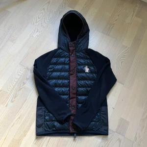 Cardigan/Jacka från Moncler - Säljer en snygg jacka/cardigan från Moncler. Jackan har en quiltad design med dragkedja och knappar framtill. Den är långärmad och har en praktisk huva. Perfekt för kyligare dagar!