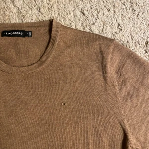Beige tröja från J.Lindeberg - Säljer en stilren beige tröja från J.Lindeberg. Tröjan är långärmad och har en diskret logga på bröstet. Perfekt för en avslappnad och elegant look. Passar bra till både jeans och chinos.
