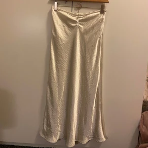 Glansig kjol - Kjol med glansigt tyg, scrunch framtill och volang vid midjan. Dragkedja vid vänstra sidan av höften. Forever21 strl S😙Perfekt till studenten! Krämvit