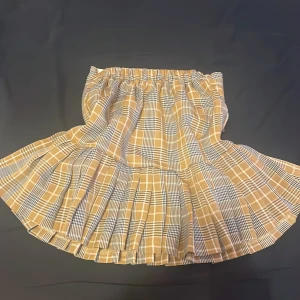Rutig kjol från King Kid - Säljer en söt rutig kjol från King Kid i beige och svart. Kjolen har en elastisk midja och ett klassiskt rutmönster som ger en tidlös look. Perfekt för att skapa en stilren outfit.