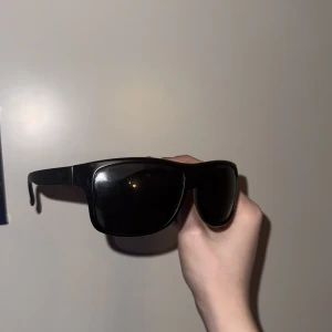 Svarta solglasögon från Emporio Armani - Snygga svarta solglasögon från Emporio Armani med en klassisk design. De har en solid svart båge och mörka linser som ger ett stilrent intryck. Perfekta för att skydda ögonen mot solen med stil.