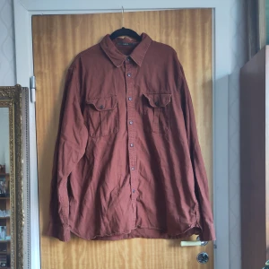 Brun skjorta med knappar - Säljer en brun ostruken långärmad skjorta från Classic Fit. Skjortan har knappar framtill och två bröstfickor med knappstängning. Perfekt för en avslappnad stil.