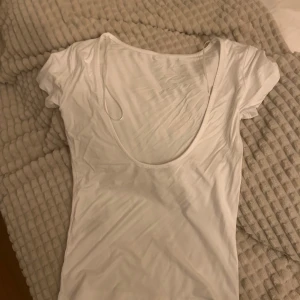 Vit kortärmad topp - Säljer en stilren vit topp med korta ärmar och rund halsringning där bak.