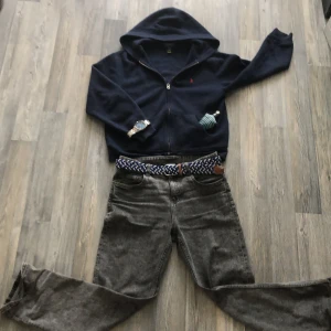 Marinblå hoodie från Ralph Lauren - Säljer en marinblå hoodie från Ralph Lauren med dragkedja och huva. Den har en broderad röd logotyp på bröstet och är tillverkad i ett mjukt material. Perfekt för en avslappnad stil. Skulle säga att den passar för alla mellan 155-167 ish då den är ganska loose. Jag säljer tröjan för att den har blivit för liten för mig och tröjan har inga defekter. ⚠️vid snabb affär är priset ej spikat i sten⚠️ Mvh Arvid👋