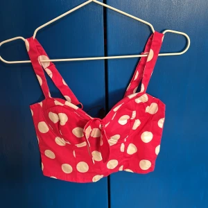 Rosa prickig croppad topp från Ann Christine - Säljer en söt rosa croppad topp från Ann Christine med vita prickar och knytning framtill. Toppen har breda axelband och en smockad rygg för extra komfort. Skön och söt, en härlig topp, aldrig använt🩷
