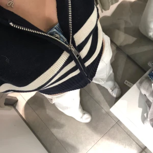 Svart och vit randig kofta med dragkedja - Snygg marinblå kofta med vita ränder och dragkedja framtill. Perfekt för en stilren look. Koftan är croppad och har långa ärmar.