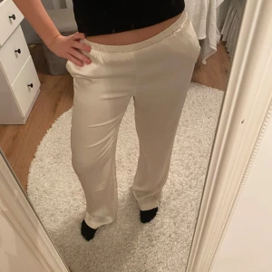 Satin byxor från bikbok - Snygga vita byxor i satin  med resårmidja för en bekväm passform. De har en rak och avslappnad stil, perfekt för en chill dag. Prislappen finns kvar och är inte alls använda utan endast testade. Passar både xs och s