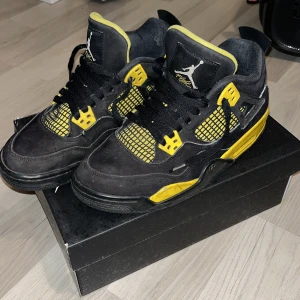 Svarta och gula Nike Air Jordans 4  - Säljer ett par svarta och gula Nike Air Jordans 4 med snörning och ikonisk Jumpman-logga. Skorna har en iögonfallande design med gula detaljer och svart bas. Perfekta för sneakerheads som vill sticka ut.