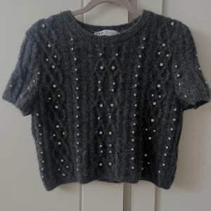 Grå stickad tröja från Zara - Säljer en grå stickad tröja från Zara med korta ärmar och pärldetaljer. Tröjan har ett fint flätmönster och perfekt för både uppklätt tillfällen eller vardagligt. Orginalpriset är 399 kr. Om någon önskar fler bilder eller har frågor är det bara att höra av sig! Tröjan är i storlek XS/S men passar båda💕