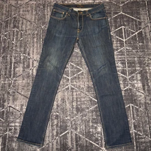 Mörkblå Jeans, Vit detaljerat på bakfickor - W32 men dem är lite tightare i storleken så skulle rekommenderas till någon som är lite mindre i kropp.                                                                 Snygga blå jeans från Nudie Jeans med klassisk femficksdesign och kontrasterande sömmar. De har en normal passform och är tillverkade i slitstarkt denim. Perfekta för en avslappnad stil.