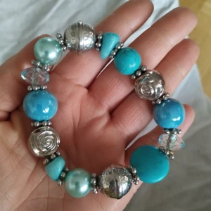 Turkost och silverfärgat armband - Snyggt armband med stora turkosa och silverfärgade pärlor. Armbandet har en mix av olika former och texturer, vilket ger det en unik look. Perfekt för att lägga till en färgklick till din outfit.