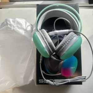Gröna hörlurar från AULA - Snygga gröna hörlurar från AULA med vadderade öronkuddar och justerbart huvudband. Perfekta för gaming eller musiklyssning. Kommer med en lång kabel för bekväm användning. Hörlurarna har en modern design med en regnbågseffekt på öronkåporna. Lyser under användning 🙂