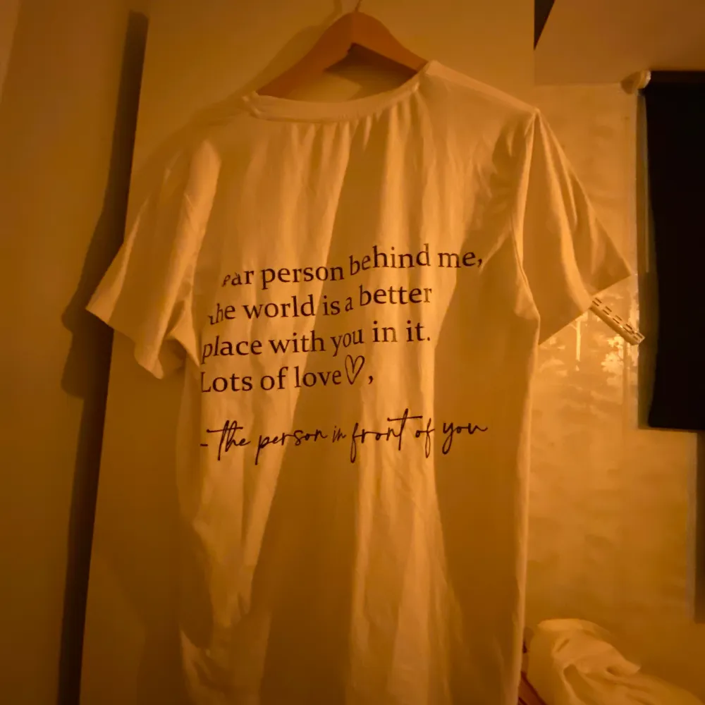 Säljer en vit t-shirt med svart text på baksidan. T-shirten har korta ärmar och är tillverkad i ett mjukt material. Perfekt för en avslappnad stil.. T-paidat.
