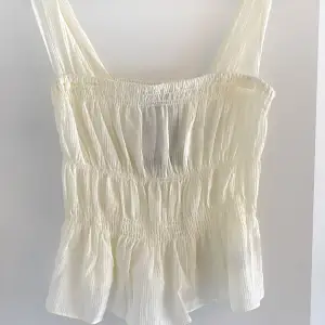 Säljer en söt vit ärmlös topp från H&M med smockdetaljer. Toppen har en luftig och lätt design, perfekt för varma dagar. Aldrig använt, prislapp kvar och ord pris 279kr