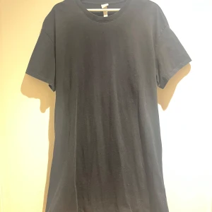 Svart t-shirt klänning  med öppen rygg  - Säljer en svart t-shirt klänning från hm med en unik design. Den har en öppen rygg med elastisk detalj och korta ärmar. Perfekt för en trendig look. 