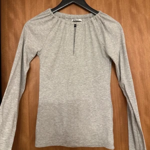Grå långärmad topp från Gina Tricot - Snygg grå långärmad topp från Gina Tricot med en diskret v-ringning. Perfekt för en stilren look. Tillverkad i ett mjukt och bekvämt material.