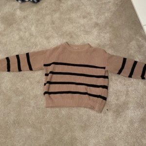 Beige och svart randig stickad tröja från Lager 157 157 - Säljer en snygg beige stickad tröja från 157 med svarta ränder. Tröjan har långa ärmar och en ribbad kant vid halsen, ärmsluten och nederkanten. Perfekt för en stilren look!