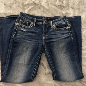 Miss me mörkblå bootcut jeans  - Säljer ett par mörkblå jeans med bootcut passform och snygga kontrastsömmar. Bakfickorna har dekorativa broderier och silvriga detaljer. Jeansen har låg midja och markerade slitningar framtill för en cool look. Pris kan diskuteras