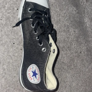 Svarta Converse Chuck Taylor All Star - Klassiska svarta Converse Chuck Taylor All Star med vit tå och sula. Skorna har snörning, rund tå och är tillverkade i canvas med gummisula. Perfekta för en avslappnad och tidlös stil. Skorna är storlek 42 och är i stort sett i nytt skick.