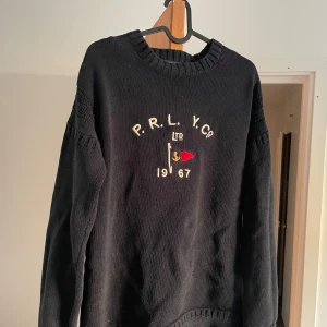 Marinblå stickad tröja från Polo Ralph Lauren - Mörkblå, grovstickad tröja från Ralph Lauren med broderi fram. Skön passform, ganska tung i materialet. Använd men i bra skick. Nypris låg runt 2500 kr.  Storlek: M