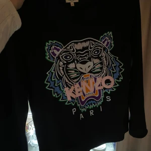Svart sweatshirt med tigertryck från Kenzo - Svart långärmad sweatshirt från Kenzo med stort broderat tigerhuvud och texten 'KENZO PARIS' på framsidan. Tröjan har rund halsringning och färgglada detaljer i broderiet. Köpt på NK Göteborg 2018, passar som storlek S/M liten i storlek🤍