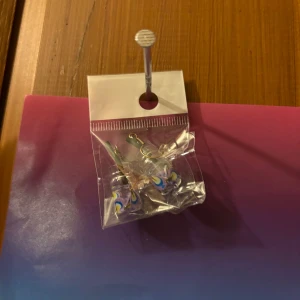 Glittriga örhängen med hjärtform - Säljer ett par glittriga örhängen i form av hjärtan. Örhängena har en regnbågsskimrande yta som reflekterar ljuset och ger en färgglad effekt. Perfekta för att addera lite extra glans till din stil!