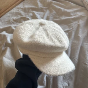 Vit ullig keps med mjuk skärm - Säljer en vit keps med mjuk, ullig känsla och rundad form. Kepsen har en bred, mjuk skärm och en klassisk design som ger en trendig look. Perfekt accessoar för att lyfta din outfit.