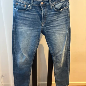 Blå jeans från Jack & Jones Tapered Mike - Säljer ett par klassiska blå jeans från Jack & Jones, modell Tapered Mike. Jeansen har normal passform upptill och smalnar av nedtill för en modern look. De har fem fickor, dragkedja och knapp i midjan.