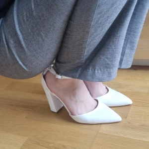 Vita pumps med klack och ankelrem - Säljer ett par stilrena vita pumps med hög blockklack och spetsig tå. Skorna har en smal ankelrem med spänne och är tillverkade i skinnimitation med slät finish. Super classy. Helt oanvända, endast provat på för bilden och dom var extremt bekväma kan jag säga. Storlek 40 ! 560kr nypris från zalando Odd and even märke student skor