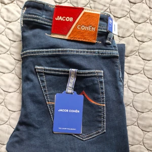 Helt Nya Jacob Cohën jeans - Snygga mörkblå jeans från Jacob Cohën med kontrastsömmar och unika detaljer som broderad text på insidan.  Amerikansk femficksmodell med knappar framtill och läderpatch bak. Perfekta för dig som gillar premiumjeans med stil. Helt Nya med Tags och Plast kvar, dessa är slim fit och perfekt för dig som skippar legday. Äkthet kan garanteras med CERTILOGO. Vid frågor om bilder, mått eller pris är det bara att höra av sig. KOM GÄRNA MED BUD