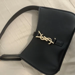 Svart axelväska - Säljer en stilren svart axelväska. Väskan har en enkel, elegant design och justerbart axelband. Perfekt för att lyfta vilken outfit som helst.