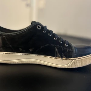 Svarta sneakers i mocka med snörning - Säljer ett par svarta lanvin i mocka som har gått sönder men funkar fortfarande. Säljer skorna pågrund av att dom har gått sönder. Priset är 500 vid snabb affär kan pris diskuteras. 