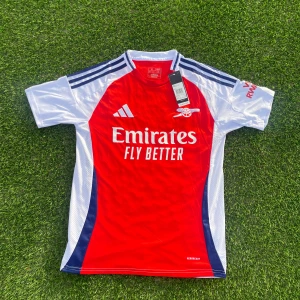 Arsenal hemmatröja Adidas 24/25 - Säljer en Arsenal hemmatröja från Adidas i rött, vitt och blått. Tröjan har korta ärmar, klassisk V-ringning och klubbens logga samt sponsortryck på bröstet. Tillverkad i lätt och ventilerande material, perfekt för match eller träning.