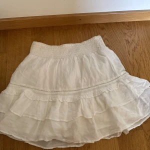 Vit volangkjol från Gina Tricot - Säljer en söt vit kjol från Gina Tricot i storlek XS. Kjolen har bred resår i midjan och flera lager volanger för en luftig känsla. Använd fåtal gånger