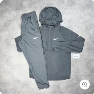 Nike tracksuit - Säljer en grå vindjacka från Nike med huva och dragkedja framtill och byxa till. Jackan har lång ärm och är tillverkad i ett lätt syntetmaterial. Perfekt för träning eller när du vill ha en sportig look.