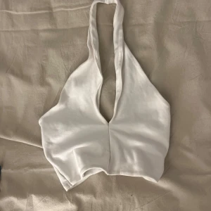 Vit halterneck linnetopp - Säljer en vit halterneck linnetopp med djup v-ringning och öppen rygg. Perfekt för varma dagar och enkel att styla till olika outfits.