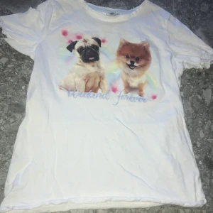 Vit t-shirt med hundmotiv från Lindex - Vit t-shirt från Lindex med tryck av en mops och en pomeranian samt texten 'Weekend Forever' i pastellfärger. T-shirten har korta ärmar och är i mjuk bomull, perfekt för dig som älskar hundar.