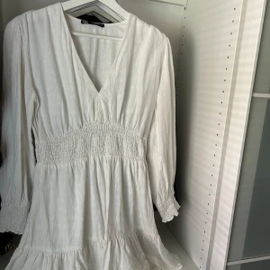 Vit v-ringad klänning från Zara - Säljer en vit klänning från Zara med v-ringning och långa ärmar. Klänningen har smock i midjan och volang nertill.. Perfekt för sommarens alla tillfällen! Skriv vid frågor! 💕