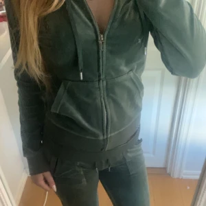 Grön Tjock tröja och Gröna mjukisbyxor från Juicy Couture - Mysig tjock tröja och gröna mjukisbyxor från Juicy Couture i velour med fickor bak och bred resår i midjan. Byxorna har en relaxed passform och klassisk Juicy Couture-logga broderad på ena fickan. Perfekta för en chill och trendig look. (Snöret satt lite löst förut så limmade fast den men inget man tänker på) kan tänka mig sälja separat 