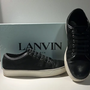 Svarta sneakers från Lanvin - Säljer ett par svarta sneakers från Lanvin med vit sula och svarta skosnören. Skorna har en klassisk låg profil och rund tå. Perfekta för dig som gillar stilrena och exklusiva sneakers.