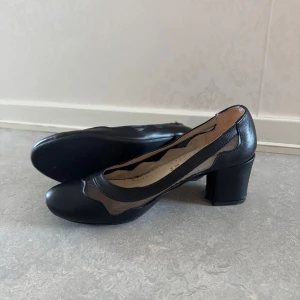 Svarta pumps med meshdetaljer från Marlop - Säljer ett par svarta pumps med rund tå och blockklack från Marlop. Skorna har snygga meshdetaljer längs sidorna och ovandelen, vilket ger en modern look. Tillverkade i syntetmaterial med en klassisk design. Har aldrig använts!