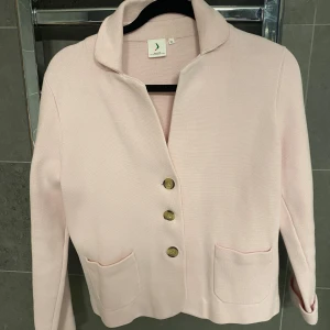 Ljusrosa cardigan jacka från Boomerang - Säljer en ljusrosa cardigan jacka från Boomerang med tre dekorativa knappar framtill och två fickor. Jackan har lång ärm, mjuk krage och är tillverkad i ett stickat material. Perfekt för lager-på-lager och en stilren look.