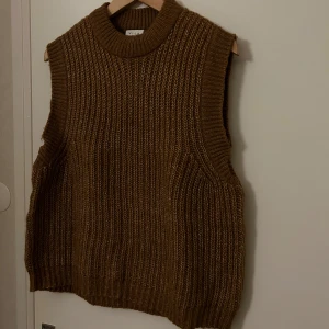 Brun stickad väst från Vila - Säljer en brun stickad väst från Vila med grov ribbstickning och hög halsringning. Perfekt att styla över en skjorta eller t-shirt för en trendig 