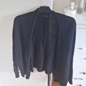 Svart stickad kofta från Åhlens - Svart stickad kofta från Åhlens i storlek M/L. Koftan är öppen framtill och har lång ärm. Perfekt att slänga på sig över en topp för en avslappnad look.