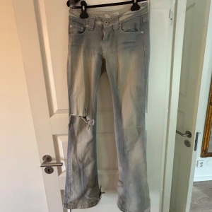 Ljusblå bootcut jeans med slitning - Säljer ett par ljusblå/grå/silver bootcut jeans med låg midja. Jeansen har dragkedja som inte går att stänga men mannkan använda säkerhetsnål!! Slitna nere vid baksidan av benet, köpte på Karlaplan loppis! Midjemått: 33 cm, innerbenslängd: 82 cm 