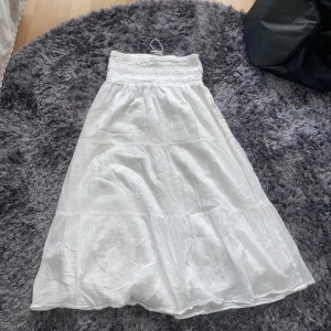 Vit långkjol från Gina Tricot - Säljer en vit långkjol från Gina Tricot med smock i midjan och lätt, luftig känsla. Kjolen har en enkel och stilren design, perfekt för varma dagar. Materialet känns mjukt och bekvämt mot huden.